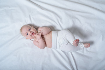 Smiling cute blond baby lying on white sheet. Top view