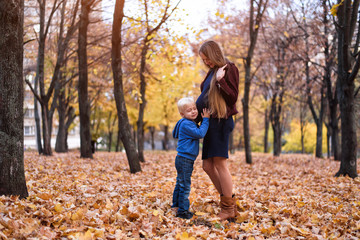 Little blond boy listening to the belly of his pregnant mother. Autumn park on the background