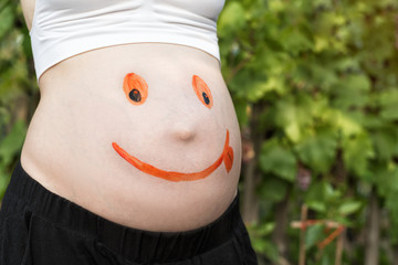 Belly of a pregnant woman with a painted smiling face. Green background