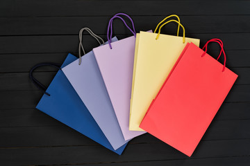 Five paper multi-colored shopping bags on black wooden background. Top view.