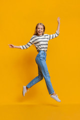 Funny teen girl walking on air, jumping over orange background