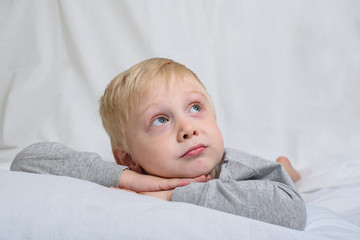 Blond boy lies with his head in his hands and looks up. White background