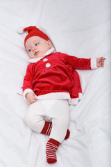 Portrait of cute little baby in a santa hat and costume. Christmas concept. Lying on white bed.
