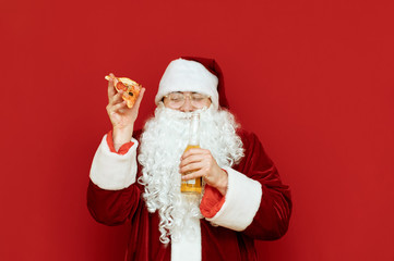 Funny man in santa claus costume isolated on red background with beer bottle and slice of pizza in hands, smiling with eyes closed. Cheerful Santa is having fun under alcohol. Copyspace