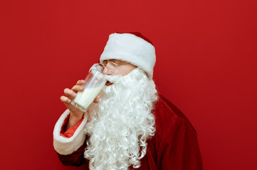 Obraz na płótnie Canvas Closeup portrait of Santa Claus drinking milk from a glass on a red background and turned away.Man in santa costume drinking milk, isolated. Christmas concept.