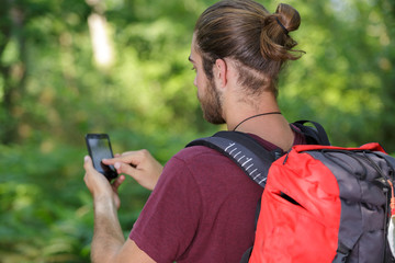 rear view of backpacker using smartphone in the countryside