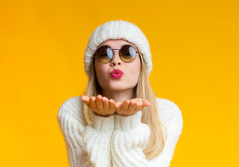 Young beautiful woman in winter hat and sunglasses blowing kiss