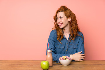 Redhead woman having breakfast cereals and fruit standing and looking to the side