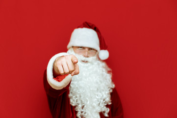 Santa Claus is standing on red background and pointing finger at camera, Santa is pointing at you. Isolated on red background. New Year and Christmas concept. Xmas