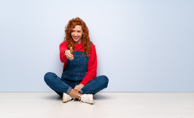 Redhead woman with overalls sitting on the floor shaking hands for closing a good deal