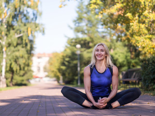 Naklejka na ściany i meble Smiling woman sitting on the pavement and stretching outdoor in urban park, selective focus