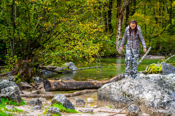 a young, red-haired girl with glasses, fashionable, sportily dressed stands in the rain, in the background an alpine lake