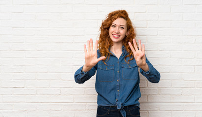 Redhead woman over white brick wall counting nine with fingers