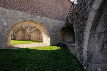 Obraz premium View of the courtyard of the old fortress. Skovoz an arch in a wall on a green lawn the sunlight falls. The yard is surrounded by thick stone walls. Citadel in the city of Besancon. France. Background