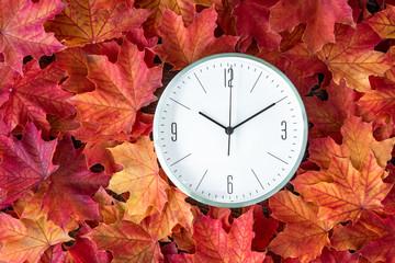 Modern clock on a background of orange and yellow maple leaves, fall time change concept