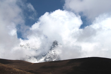 Fototapeta na wymiar Kyajo Ri mountain peak is visible through dense white clouds in Himalayas in Sagarmatha national park in Nepal near Lunden village. On the way to Everest base camp through Gokyo lakes.