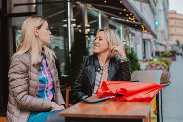 Two young women friends met in a city street cafe and have fun chatting.