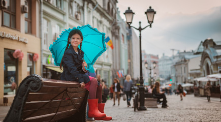 Fototapeta na wymiar Little girl 6 years old child with an umbrella in rubber boots having fun on a bench in the center of Moscow in the fall or spring.