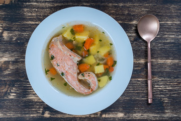 Fresh salmon fish soup with carrots and potatoes in a white plate, close up
