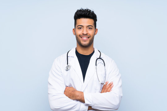 Young doctor man over isolated blue wall smiling a lot