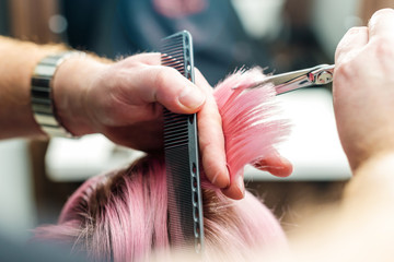 Close up of hairdresser's hands are cutting pink tips while getting rid of split ends at hair salon. Beauty hairstyle concept.