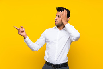 Young handsome man over isolated yellow background surprised and pointing finger to the side