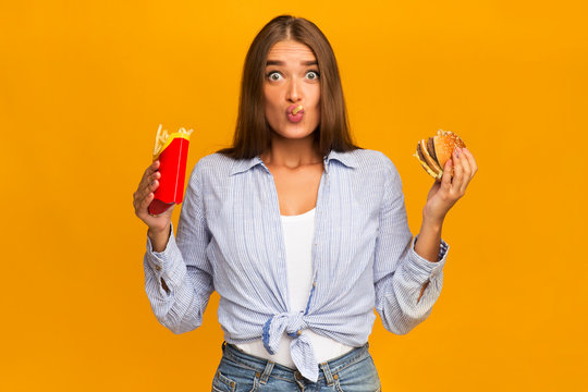 Surprised Woman Eating Burger And French Fries, Studio Shot
