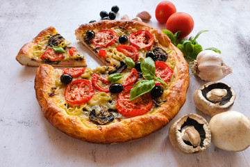  Vegetarian homemade pizza on a light background with a cut piece. Next ingredients -mushrooms, tomatoes, garlic, Basil, olives.   The concept of healthy eating.
