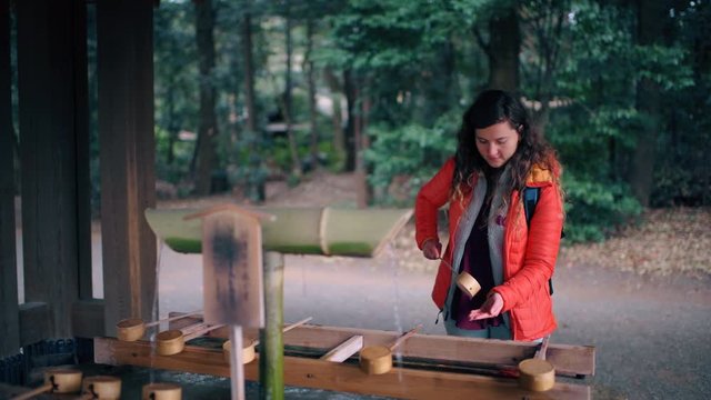 Tokyo, Japan Meiji shrine entrance water purification fountain with tourist caucasian woman during spring praying purifying hands