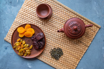 Clay teapot, cup, green tea, dried fruits in a clay plate stand on a mat