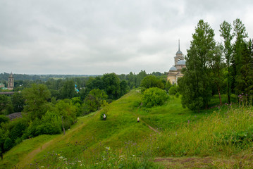 A hill covered with green grass, a path and a Church at the top, hidden behind trees.