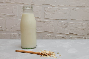 Dairy-free vegan oat milk in a glass bottle with oat flakes on grey background, copy space