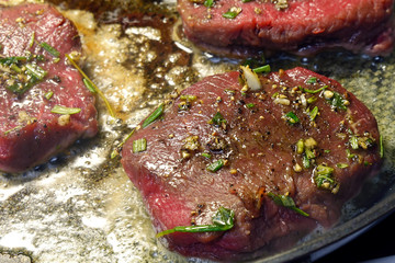 Venison steaks on frying pan. Deer meat sirloin is spiced with garlic, rosemary and thyme.