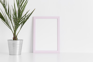 Pink frame mockup with a palm in a pot on a white table.Portrait orientation.