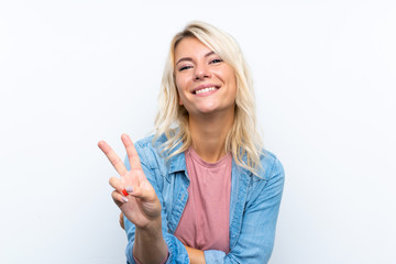 Obraz premium Young blonde woman over isolated white background smiling and showing victory sign