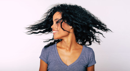 I whip my hair back and forth. Charming Afro-American lady with frizzy dark hair is whipping her hair with her eyes closed while laughing with joy.