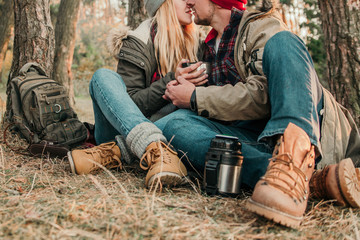 Travel couple camping with thermos in the forest. Concept of trekking, adventure and seasonal vacation.