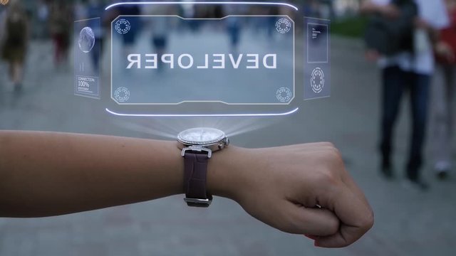 Female hand with futuristic smartwatch shows HUD hologram with text Developer. Woman uses holographic technology of future on wristwatch against background of evening city with people