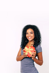 Golden ribbon. Front portrait of terrific African ethnic woman with frizzy black hairstyle and luminous smile who is holding a small heart-shaped box near her chest.