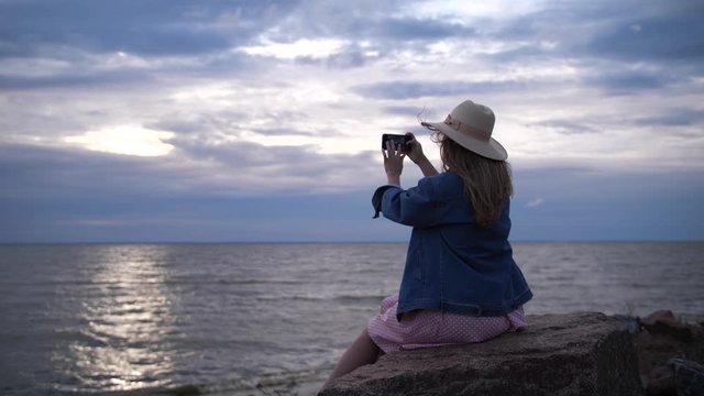 The girl in the hat takes pictures of the sunset on the sea. 4K Slow Mo