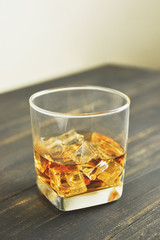 glass of whiskey with ice cubes on wooden table