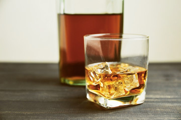 glass of whiskey with ice cubes on wooden table