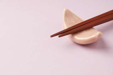 Wooden chopsticks and chopstick rest on bright paper background. Close up. Copy space. 