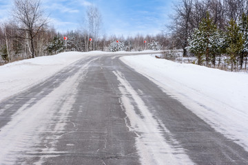 Patterns on the winter highway in the form of four straight lines. Snowy road on the background of snow-covered forest. Winter landscape.