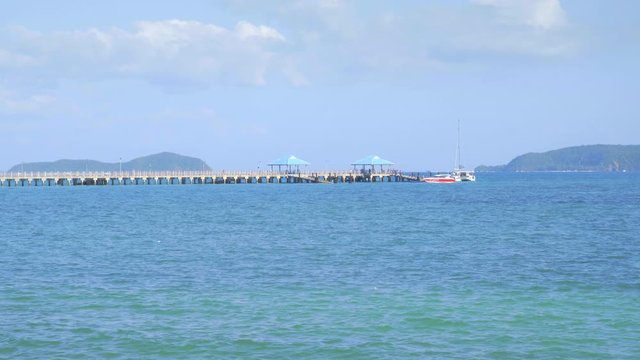 People are walking in pier from small boat in bright blue water near tropical beach