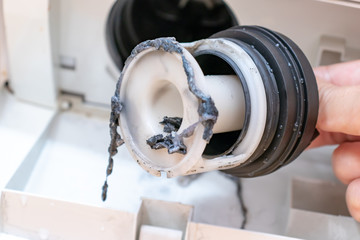 Inspecting washing machine's dirty clogged drain pump filter close up, clean and repair