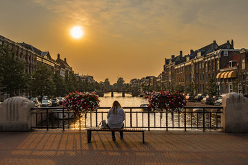 Fototapeta na wymiar Sunrise over a canal at a windmill in the Netherlands Amsterdam. A lone woman on a bench on a bridge