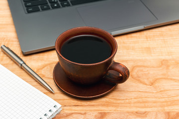 Work wooden office table with laptop, coffee cup, notepad and pen