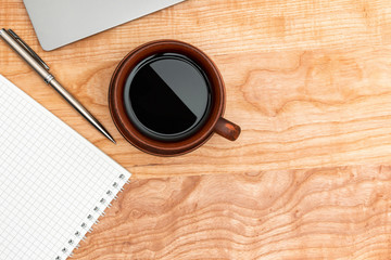 Work wooden office table with laptop, coffee cup, notepad and pen, top view