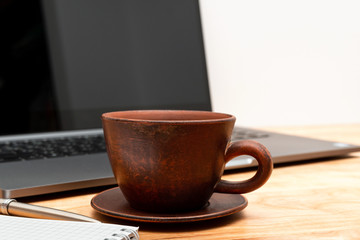 Work wooden office table with laptop, coffee cup, notepad and pen